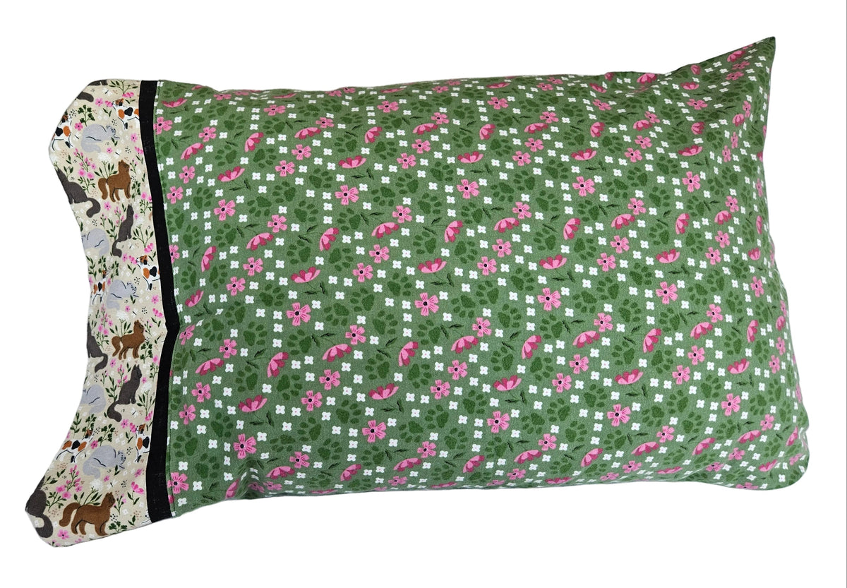 A rectangular pillowcase with a green, pink, and white patterned design, featuring a solid black border and a cat patterned cuff